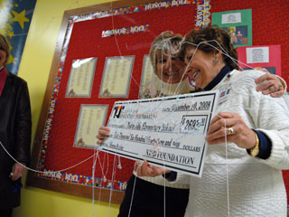 Two ladies hug each other and celebrate as a scholarship check is presented